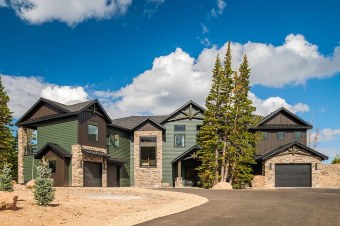 Grand front exterior of a custom mountain lodge home in Brian Head, UT by Choice Builders, with green and black siding, stone accents, and a spacious driveway