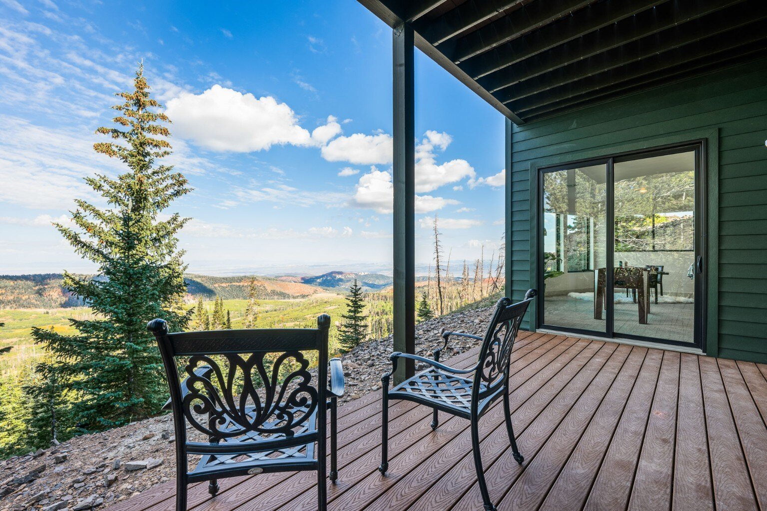 A breathtaking view of the mountains from the patio of a custom mountain lodge home in Brian Head, UT by Choice Builders, featuring stylish black chairs and a wooden deck