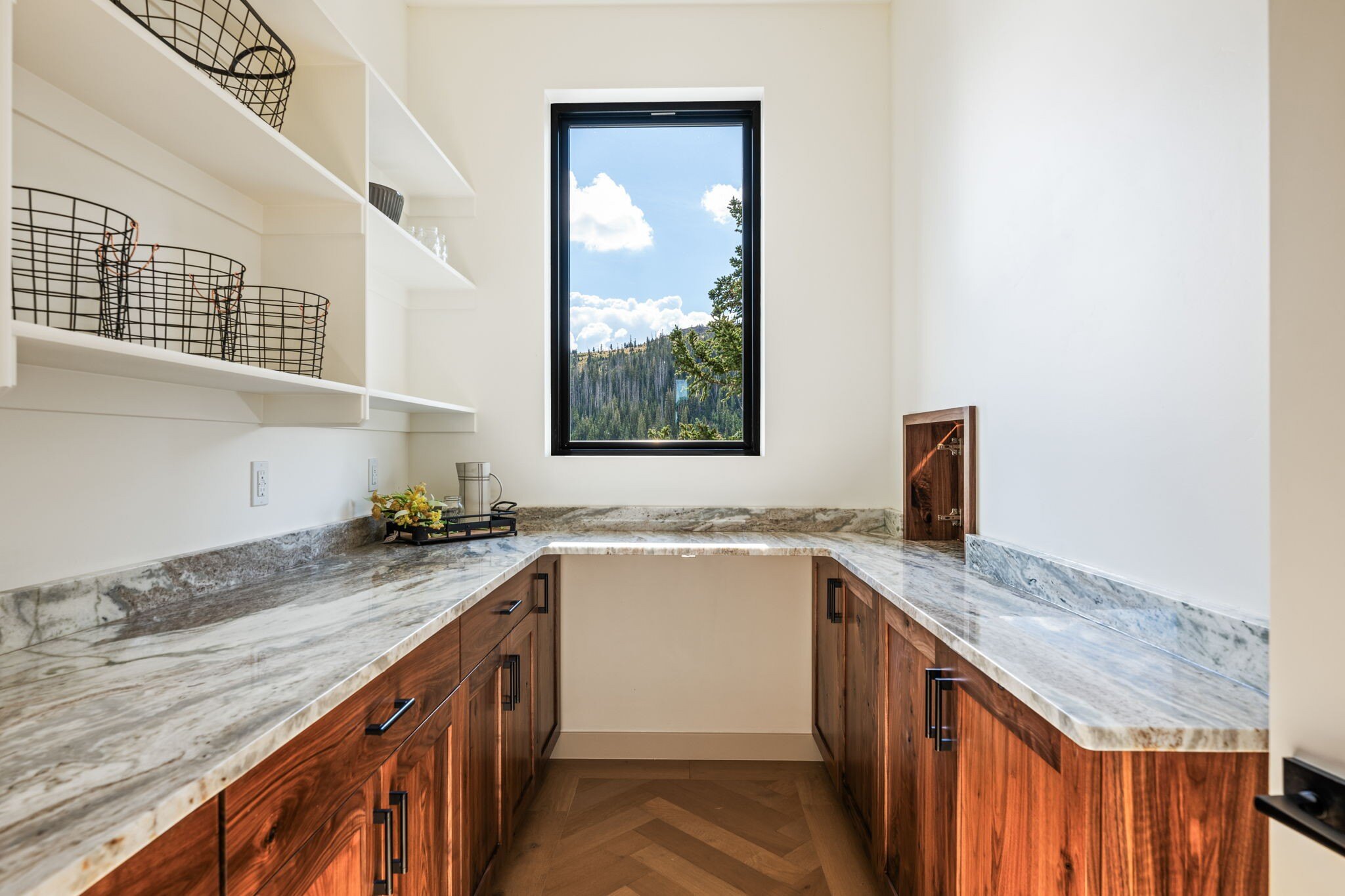 Bright and spacious pantry with marble countertops, natural wood cabinets, and a scenic mountain view in a custom mountain lodge home in Brian Head, UT by Choice Builders