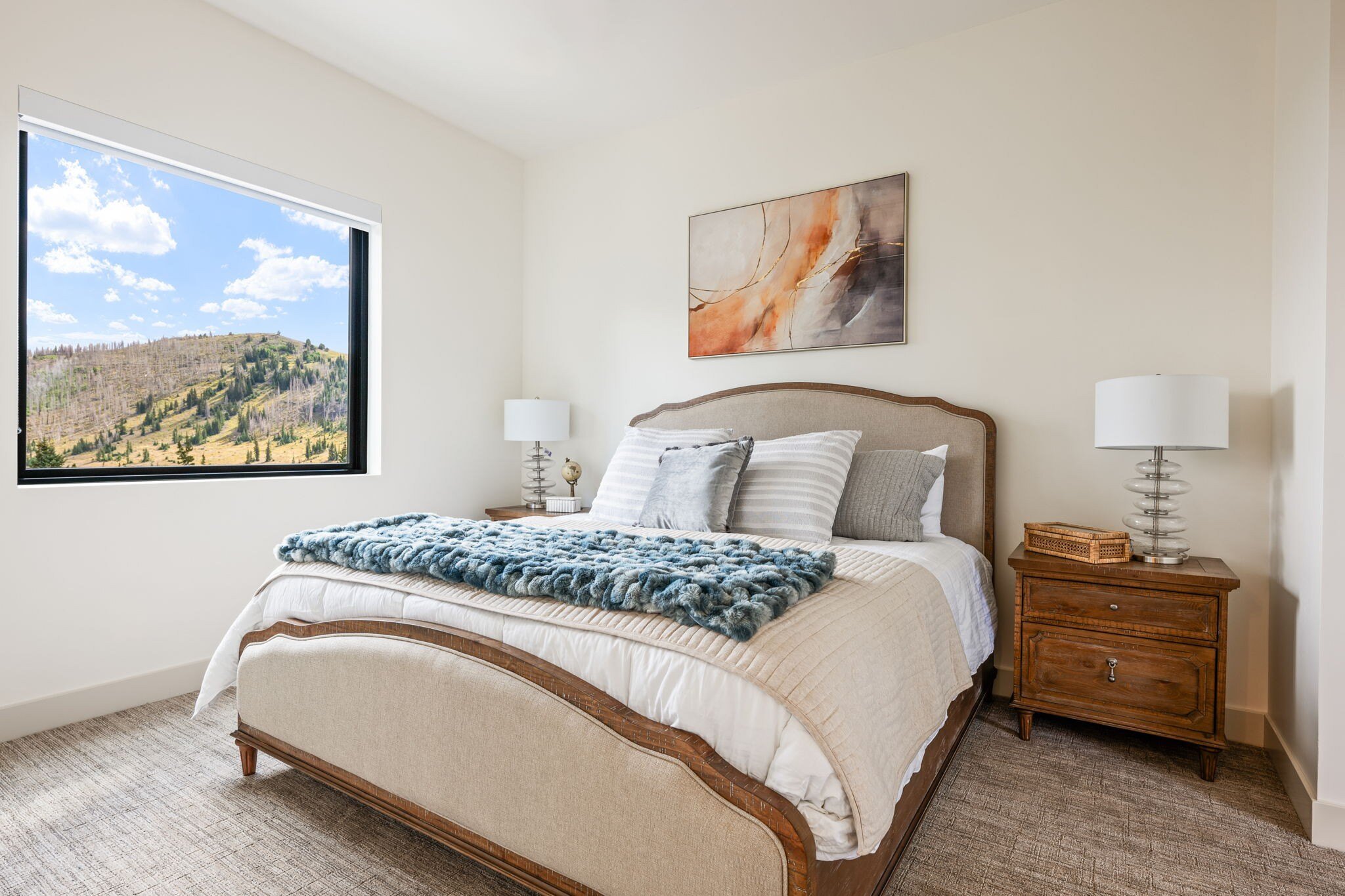 Cozy bedroom with a large picture window overlooking the mountains, featuring a neutral-toned bed and wooden nightstands in a custom mountain lodge home in Brian Head, UT by Choice Builders