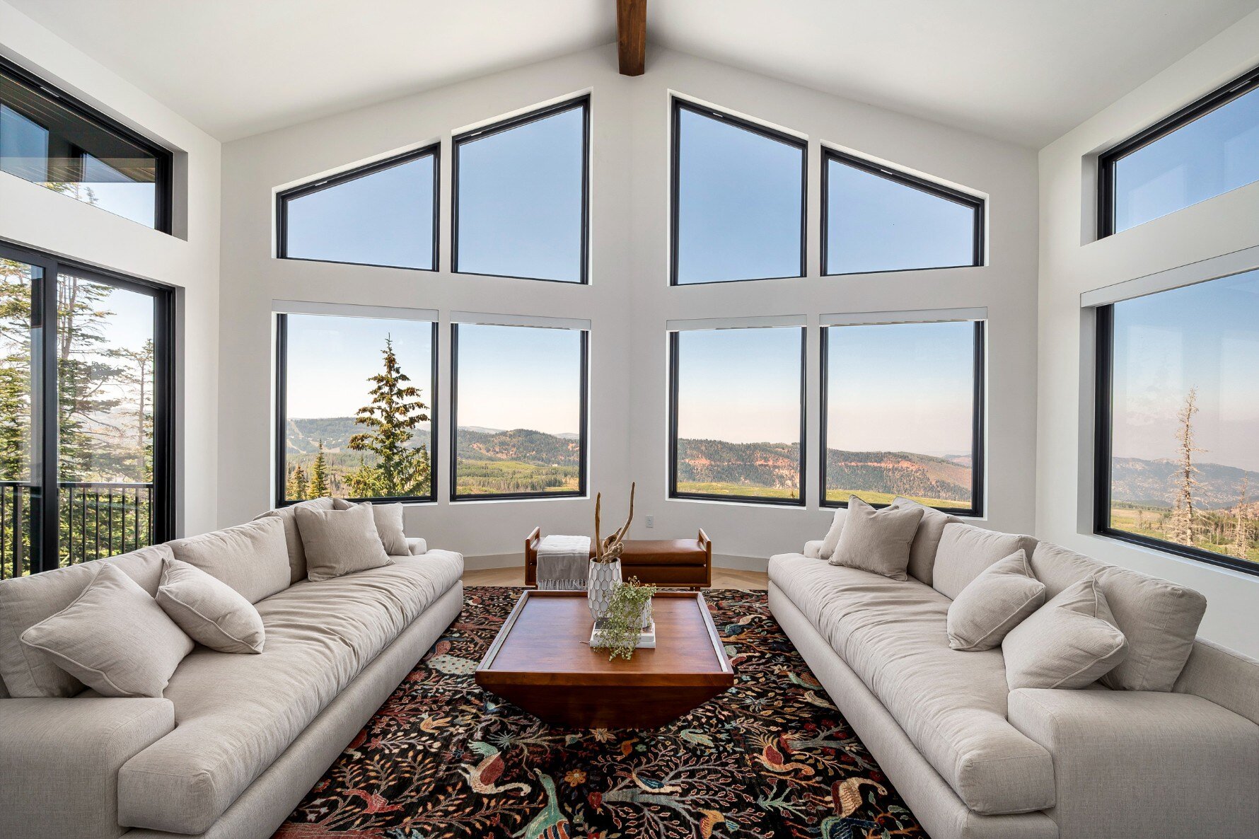 Elegant living room with large windows showcasing panoramic mountain views, complete with neutral-toned sofas and a decorative rug in a custom mountain lodge home in Brian Head, UT by Choice Build