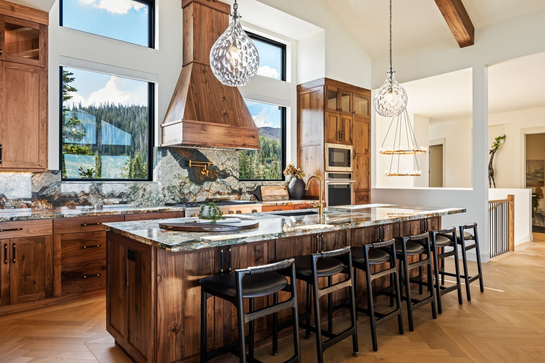 Luxurious kitchen featuring a granite island, modern appliances, and large windows with forest views in a custom mountain lodge home in Brian Head, UT by Choice Builders