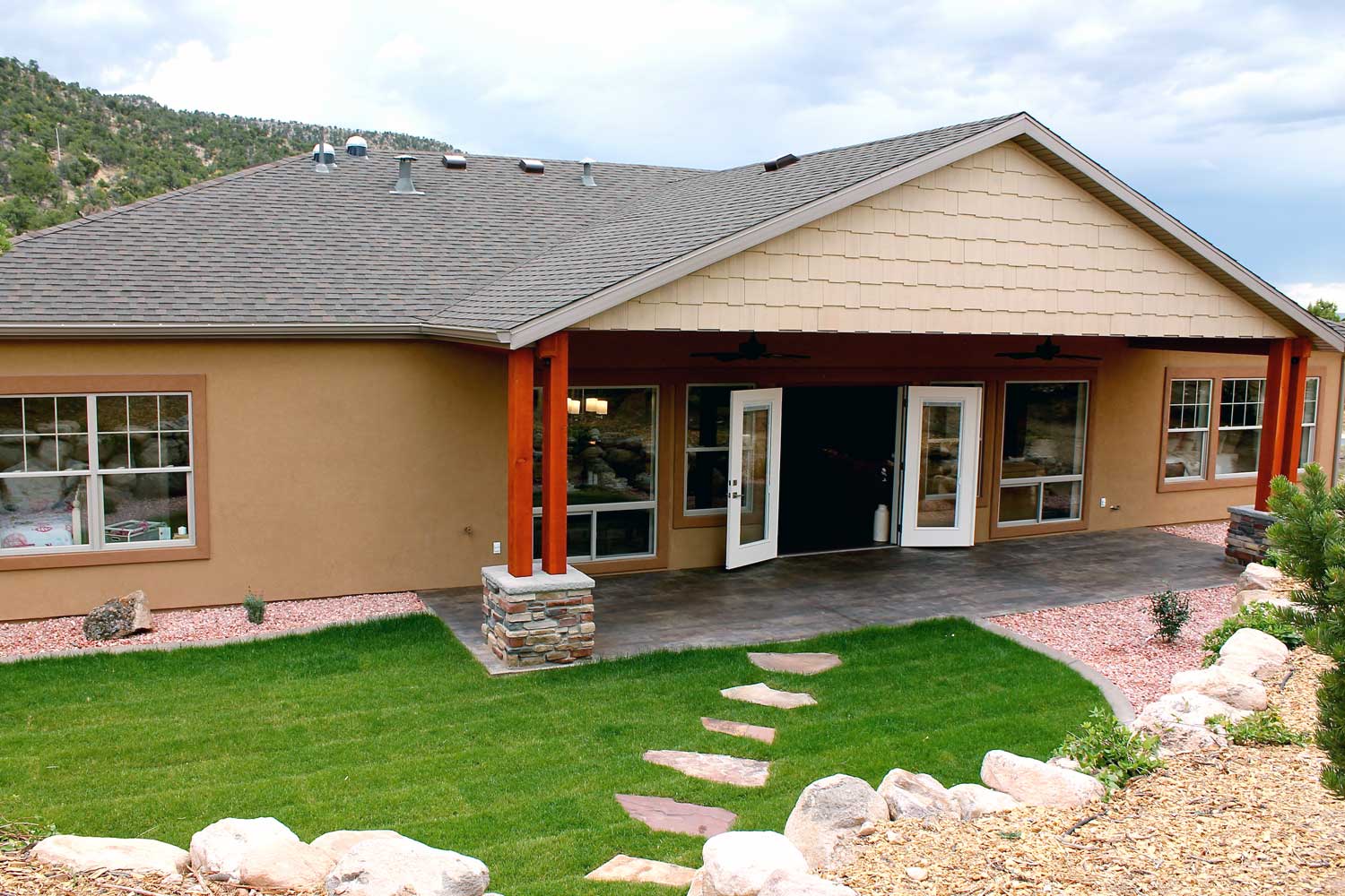 back patio exterior with french doors open to living room, green grass, rock wall, stepping stones leading to entrance
