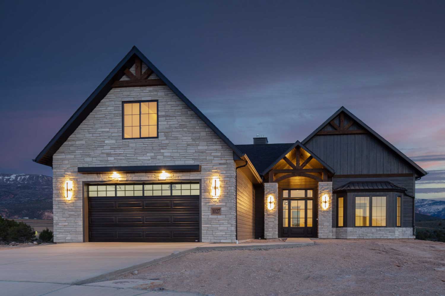 Front view of custom home at dusk featuring outdoor lighting that highlights the stone and wood exterior